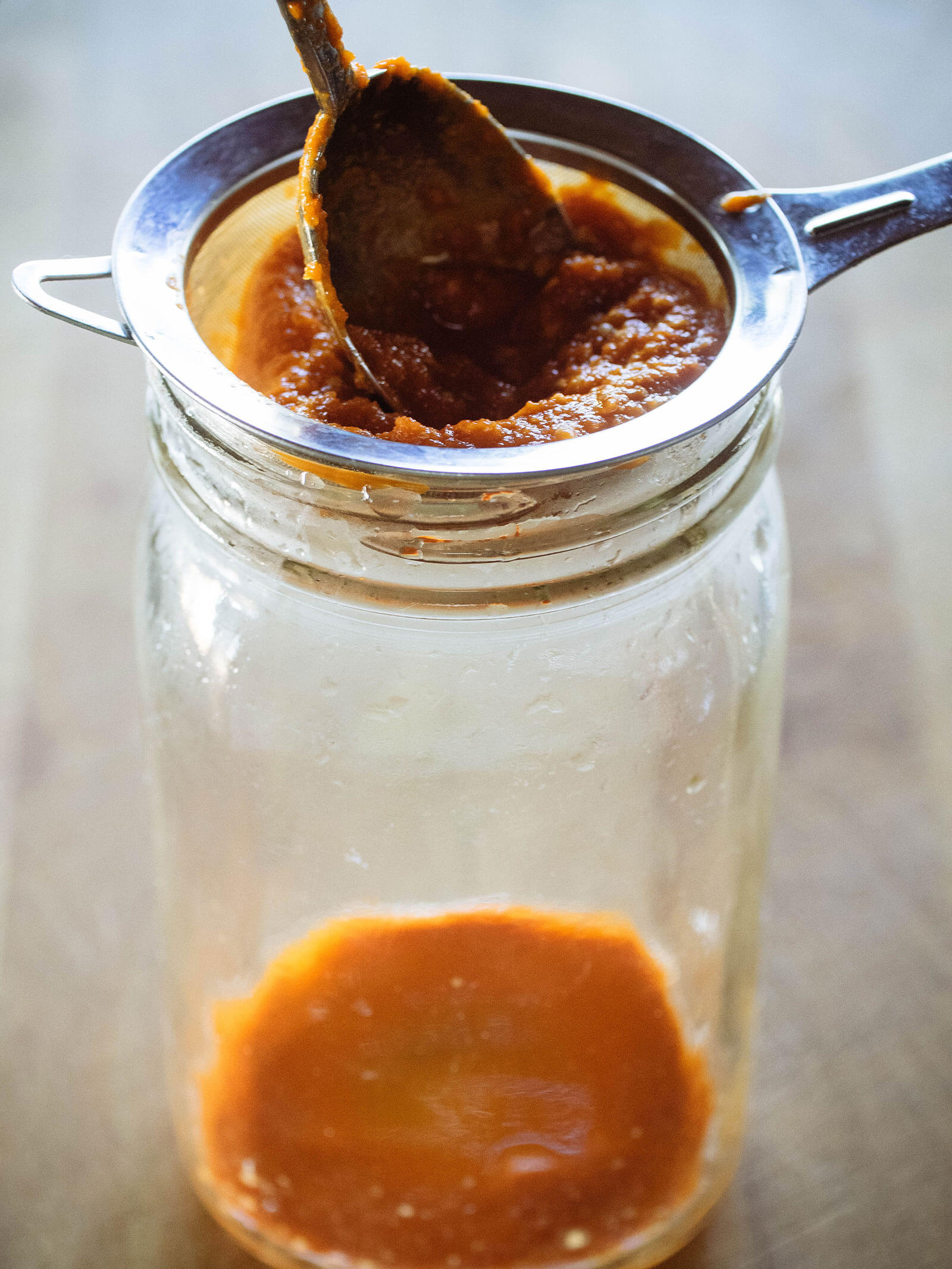 Fermented hot peppers being strained in a jar to make hot sauce