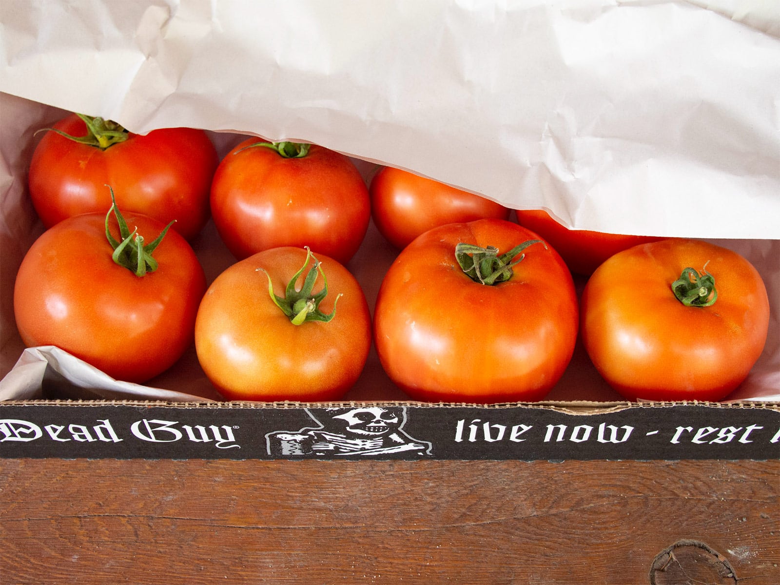 A cardboard flat of large red tomatoes covered with sheets of paper